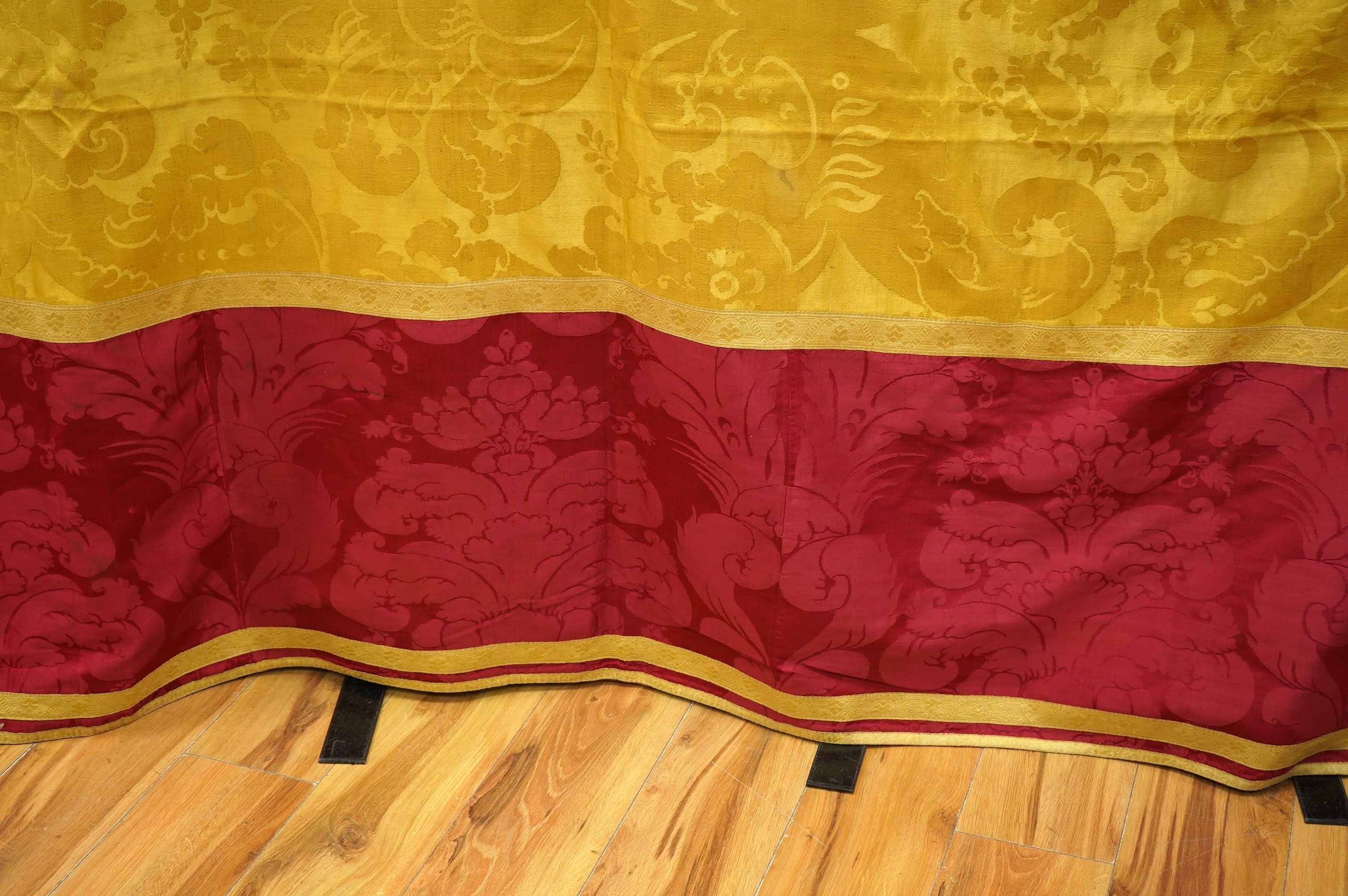 A 19th century gold and crimson silk damask bed cover, the centre being short loom widths of gold damask in a large repeating design, the outer panel a similar crimson damask, both finished with decorative gold braid bor